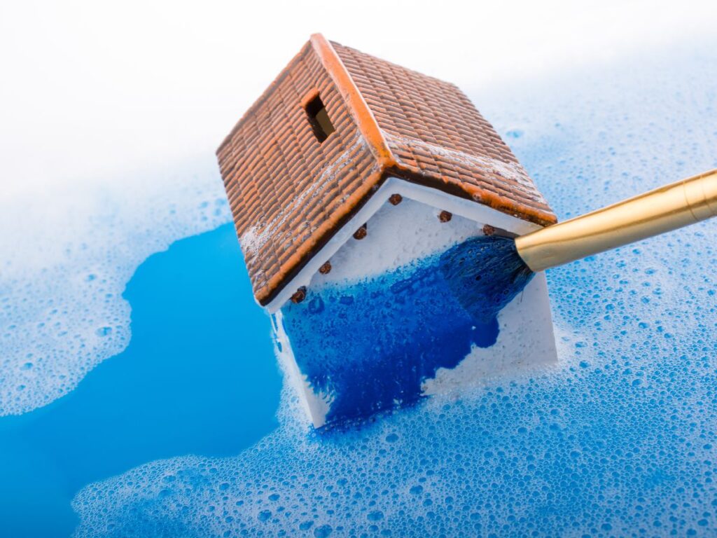 Small house model being painted blue with a brush in foamy liquid
