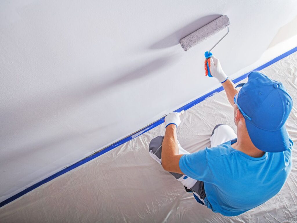 Painter rolling white paint across an interior ceiling