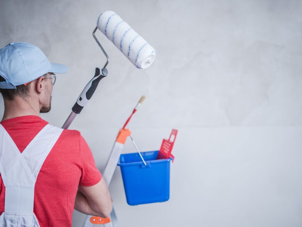 Painter holding a roller beside a bucket and ladder