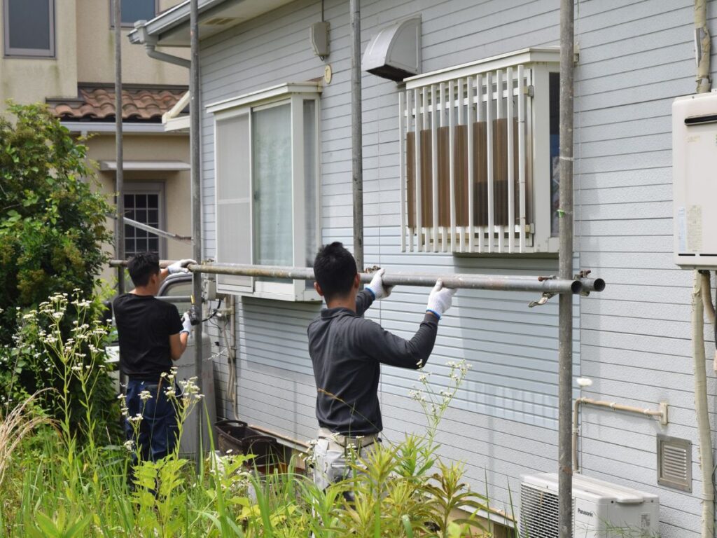 Workers setting up scaffolding beside a house exterior