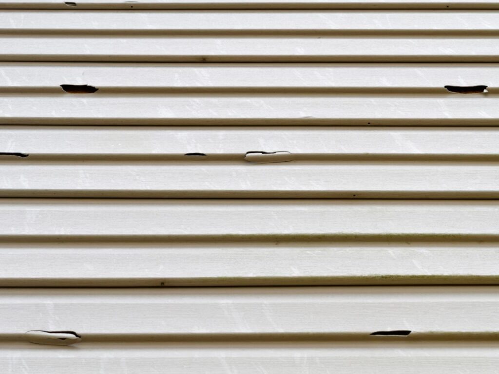 Close-up of damaged vinyl siding with cracks and holes